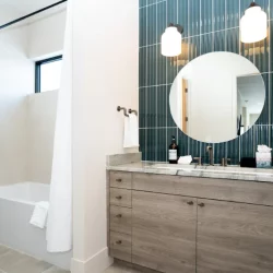 blue tile behind round mirror vanity with glimps of tub/showe in background